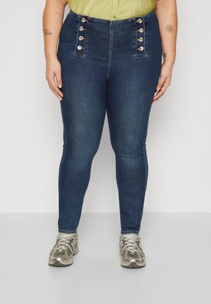 Höga denimjeans i mörkblått med silverfärgade knappar på framsidan, figursydda ben och subtilt strukturerad yta.
