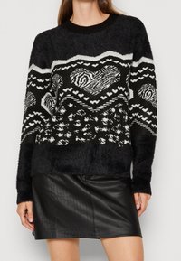 Schwarz-weißer gemusterter Pullover mit einer flauschigen Textur, der Herzen und geometrische Formen zeigt, kombiniert mit einem schwarzen Lederrock.