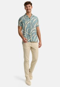 Button-up shirt with a light blue background and cream botanical pattern, paired with beige pants and light sneakers. Smooth fabric, short sleeves.