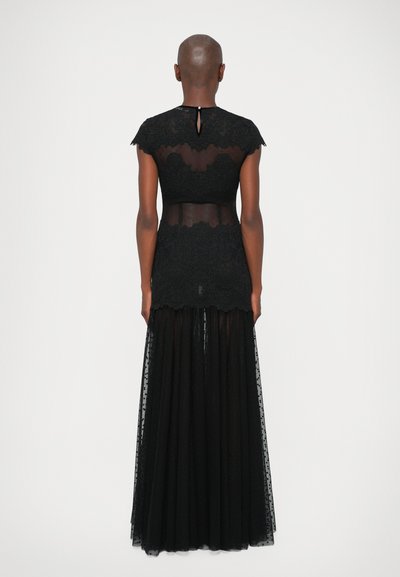 Črna obleka z čipkastim zgornjim delom in prosojnim hrbtom, kratkimi rokavi in dolgo, lepršavo tila krilo z pikastim vzorcem. Detajl v obliki ključavnice na izrezu.