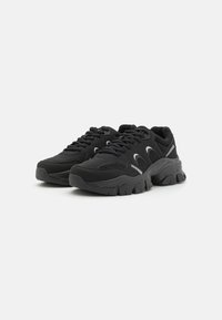 Baskets de sport noires en maille et matériau synthétique, dotées d'une semelle épaisse, d'une forme arrondie et d'accents réfléchissants. Modèle à lacets.