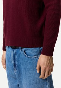 Vinröd stickad tröja med ribbad struktur och åtsittande mudd, kombinerad med ljusblå denimjeans som visar upp en avslappnad passform och klassisk skärning.