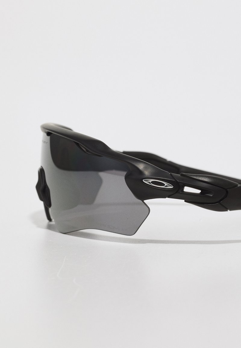 Black sports sunglasses with gray tinted lenses, aerodynamic design, and rubber grips for comfort, featuring an emblem on the side.