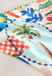 Tkanina z kolorowymi tropikalnymi i geometrycznymi wzorami, w tym z palmą, niebieskimi liśćmi, czerwonym szachownicowym wzorem i abstrakcyjnymi kształtami.