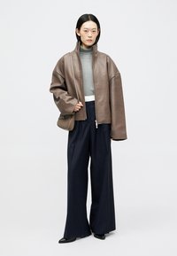 Καφέ δερμάτινο υπερμεγέθη μπουφάν, γκρι ζιβάγκο, φαρδιά μπλε παντελόνια με λεπτές ρίγες, μαύρα μυτερά παπούτσια και μικρή τσάντα ώμου.