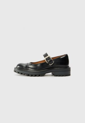 Chaussure Mary Jane en cuir noir avec semelle épaisse à crampons et bride à boucle argentée sur fond neutre.