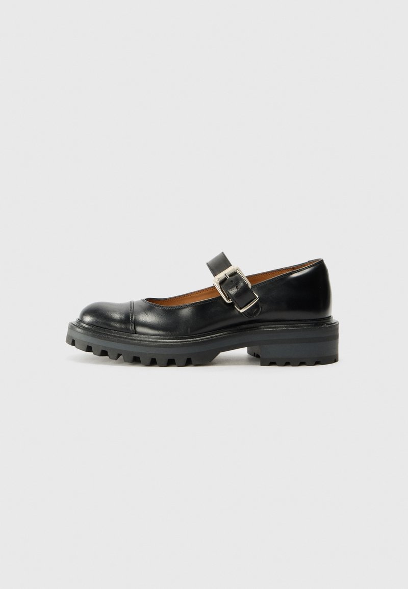 Chaussure Mary Jane en cuir noir avec semelle épaisse à crampons et bride à boucle argentée sur fond neutre.