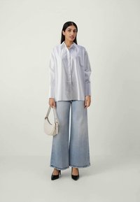 Chemise blanche oversize avec un col pointu, associée à un jean large bleu clair. Les accessoires comprennent un petit sac à main blanc et des talons noirs.