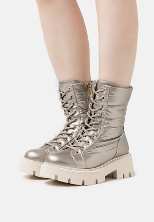 Metalliske sølvfarvede snørestøvler med polstret skaft, chunky hvid sål og sidelås. Har forstærkede snørehuller og glat tekstur.