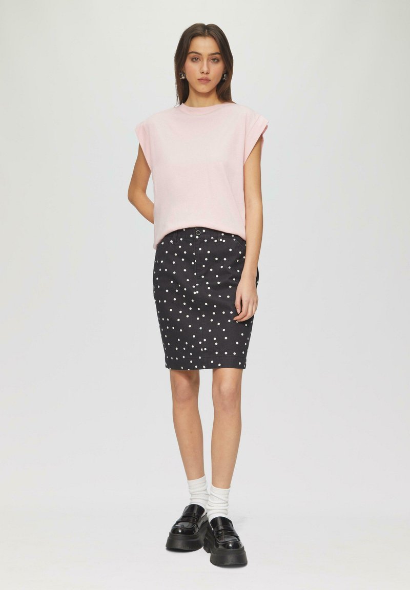  Lichtroze oversized top met korte mouwen, gecombineerd met een zwarte kokerrok met stippen, witte sokken en zwarte platform instappers.