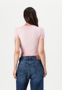 Light pink, short-sleeve cropped top with a ribbed texture paired with blue high-waisted jeans featuring back patch and pocket detailing.
