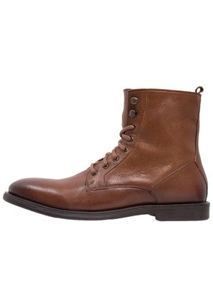 Brauner Leder-Stiefelette mit Schnürung, seitlichen Ösen und flacher dunkler Sohle, rechte Seitenansicht vor weißem Hintergrund.