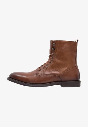 Bottine à lacets en cuir marron avec œillets latéraux et semelle plate foncée, vue de profil droit sur fond blanc.