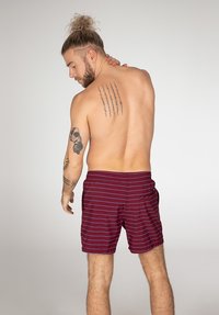 Bordeauxgestreepte zwemshorts met een elastische tailleband, zijzakken en een gladde textuur. Model getoond van achteren, met zichtbare tattoo's.