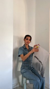 Gjennomsiktig plastpose med "Jared London" trykt i svart, holdt av en person i en denim jumpsuit. Lys bakgrunn og en trebord.