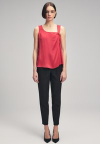 Rød satin tank top med firkantet udskæring og detaljer med knude i siden, parret med sorte skræddersyede bukser og spidse sorte hæle.
