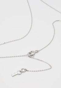 Sølvmetal halskæde med en fin kæde med cirkulære led og en nøglecharme, der viser et minimalistisk design og en glat overflade.