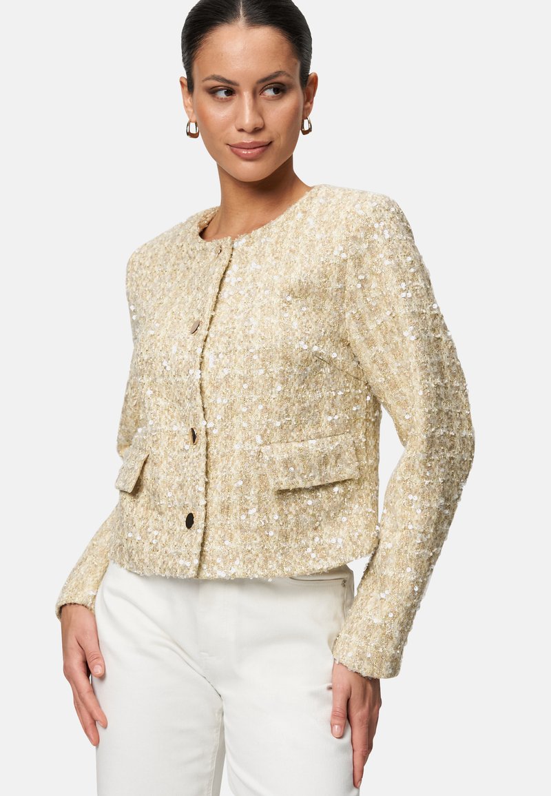 Giacca beige con paillettes, dalla finitura testurizzata, scollo rotondo, chiusura a bottoni e due tasche frontali, progettata con una silhouette accorciata.