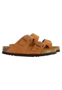 Sandales en daim beige avec deux sangles ajustables et boucles en métal argenté. La semelle en liège et la semelle extérieure en caoutchouc présentent un motif texturé.