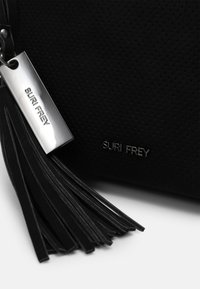Czarna torba ze skórzanej perforowanej, z metalową etykietą w kolorze srebrnym i detalami w postaci czarnej frędzli. Na boku znajduje się tłoczone logo "SURI FREY".