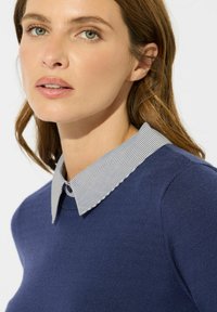 Granatowy sweter z paskowanym kołnierzem, charakteryzujący się miękką fakturą i dopasowanym krojem. Kołnierz uzupełnia okrągły dekolt ubrania.