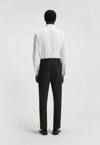 Witte overhemd met lange mouwen en een klassieke kraag, gecombineerd met zwarte op maat gemaakte broek. De outfit heeft een gladde textuur en een getailleerde silhoeët.