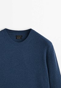 Pull bleu marine texturé avec un col rond et des poignets côtelés. Présente une étiquette à l'intérieur du col. Le matériau semble doux et en maille.