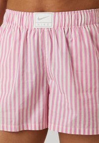 Pantalones cortos a rayas rosa y blanca con cinturilla elástica y etiqueta del logo de Nike. Fabricados con un material ligero, presentan un ajuste holgado.