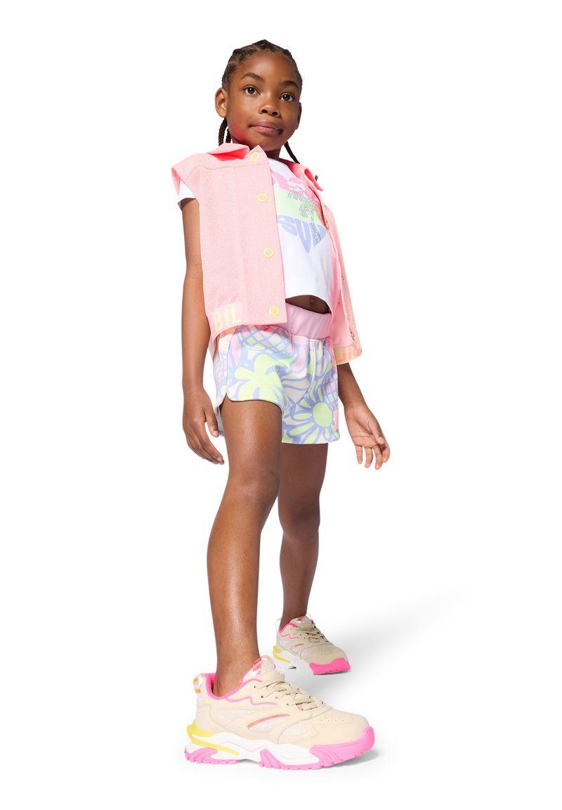 Enfant portant une veste sans manches rose clair, un t-shirt blanc à motif, un short à motifs et des baskets beige avec des accents roses.