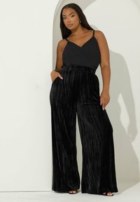 Zwarte camisole met dunne bandjes, gecombineerd met hooggeprijsde, geplooide zwarte fluwelen wijd-uitlopende broeken. Gladde textuur met zakken.