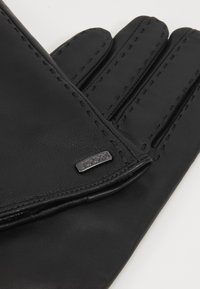 Black leather gloves with stitched detailing, featuring a silver metal logo accent. Smooth texture and classic design.