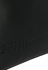 Czarna torebka z teksturowanej skóry z wytłoczonym logo "DENIM TOM TAILOR"; prostokątny kształt, gładkie krawędzie i brak widocznych detali metalowych.