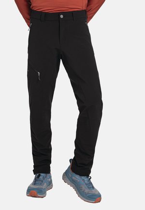 Schwarze Sporthose mit einem figurbetonten Design, ausgestattet mit seitlichen Reißverschlusstaschen und einer glatten Textur, kombiniert mit blauen und grauen Wanderschuhen.