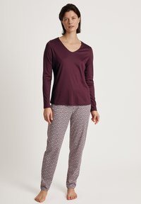 Bordeaux langharige top met een v-hals en gemusterde pyjamabroek met een geometrisch ontwerp in rood en wit op een beige achtergrond.