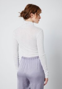 Světle šedý svetřík s dlouhým rukávem a rolákem z průhledného materiálu, v kombinaci s měkkými levandulovými kalhotami s elastickým pasem. Hladká textura, přiléhavý střih.