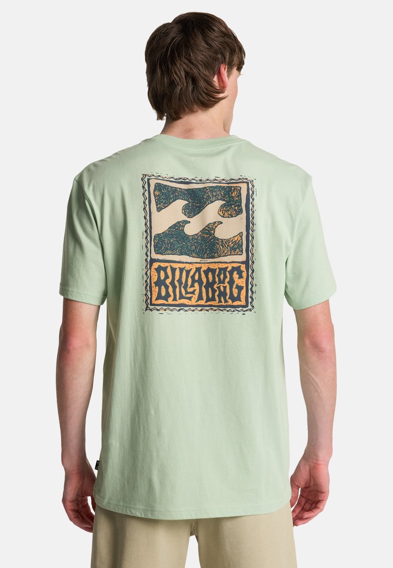 Ανοιχτό πράσινο βαμβακερό μπλουζάκι με μεγάλο γραφικό σχέδι ο με μπλε κυματιστά μοτίβα και πορτοκαλί κείμενο "Billabong" στην πλάτη. Κοντά μανίκια.