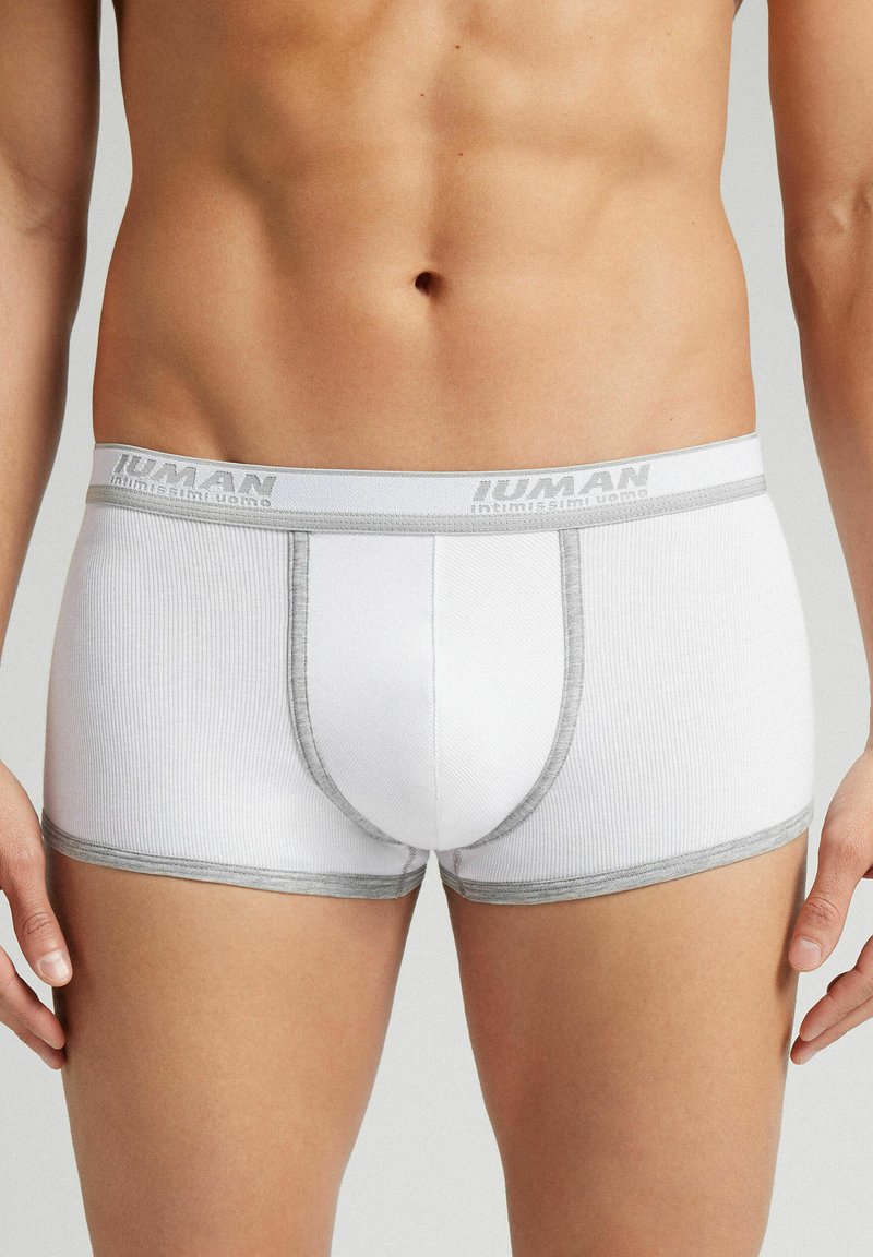 Białe bokserki z prążkowanym wzorem i szarym wykończeniem. Posiadają logo na pasku oraz przednią kieszonkę dla wsparcia.