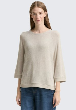 Beige gebreide trui met een ronde halslijn, driekwart mouwen en geribbelde zoom, gecombineerd met blauwe jeans. Zachte, gestructureerde stof.