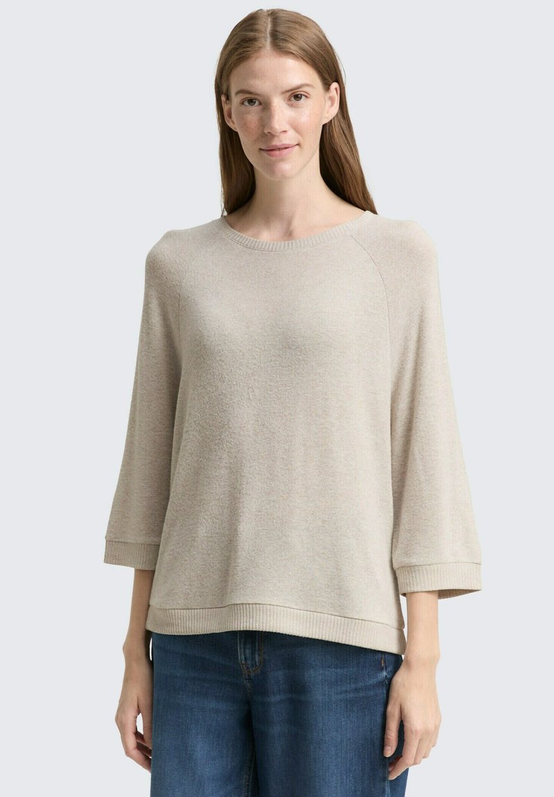 Maglione beige a maglia con scollo rotondo, maniche a tre quarti e orlo a coste, abbinato a jeans blu. Tessuto morbido e con texture.