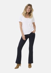 Vit kortärmad t-shirt kombinerad med mörkblå utsvängda jeans och beige klackstövlar. Avslappnad outfit med en lös passform och minimalistisk design.