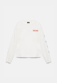 Chemise blanche à manches longues avec texte rouge "INNER SIGNAL Your energy speaks first" sur la poitrine et motifs d'étoiles bleues le long de la manche droite.