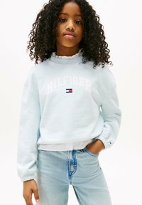 Jasnoniebieska bluza z białym napisem "HILFIGER", z prążkowanym dekoltem i elastycznymi mankietami, w połączeniu z jasnoniebieskimi dżinsami.