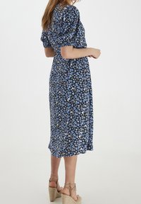 Blommig midi-klänning med en marinblå bakgrund som har små blå, gröna och vita blommor. Puffärmar och kolumnsiluett.