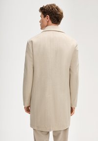 Beiger Fischgrätenmantel mit strukturiertem Kragen und Seitentaschen, mit gerade geschnittenem Design und weicher Stofftextur.