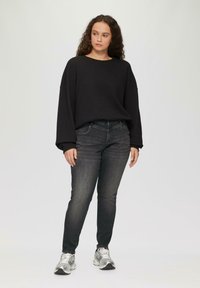 Zwarte gebreide trui met verlaagde schoudernaden, gecombineerd met donkere jeans en zilveren sport schoenen. Eenvoudig, ontspannen ontwerp met een gezellige textuur.