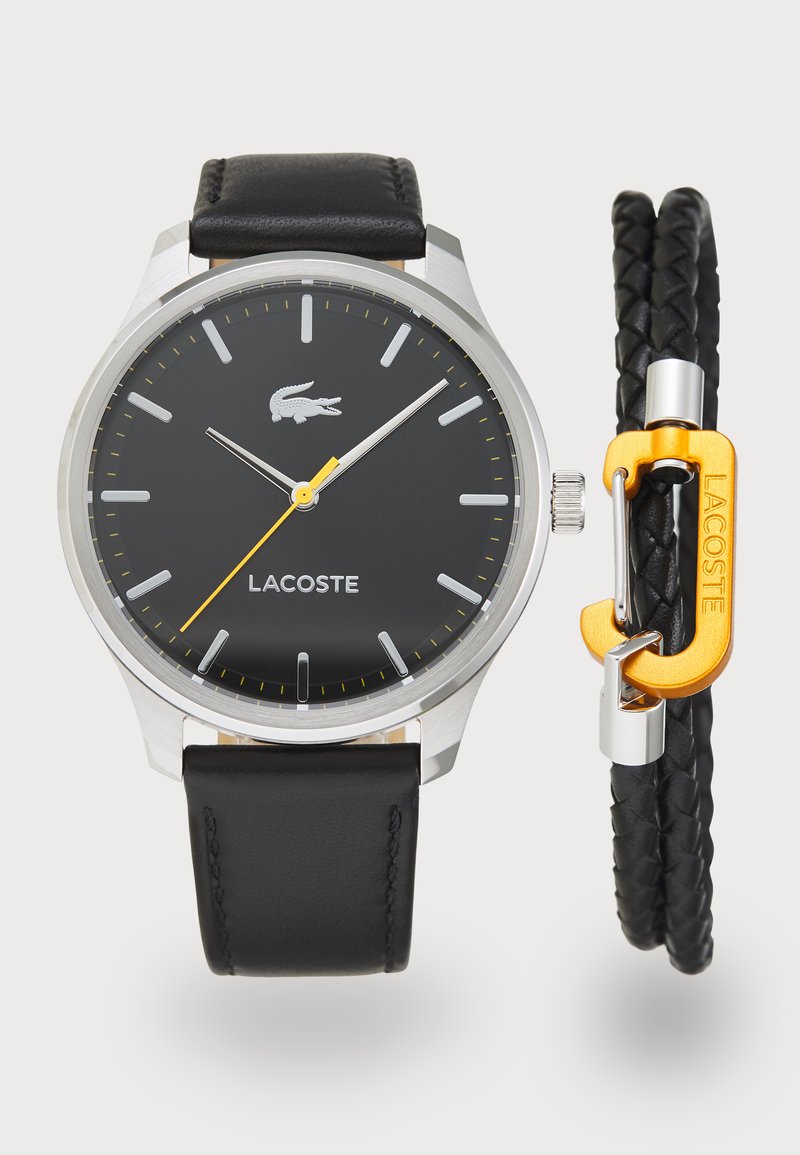 Svart läderrem klocka med silverhölje, svart urtavla, silvervisare och gula detaljer. Inkluderar ett flätat svart armband med orange spänne.