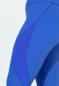 Niebieskie legginsy wykonane z rozciągliwej, teksturowanej tkaniny o kontrastujących odcieniach i szwach. Projekt wyróżnia się unikalnym panelem po bokach.