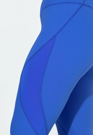 Niebieskie legginsy wykonane z rozciągliwej, teksturowanej tkaniny o kontrastujących odcieniach i szwach. Projekt wyróżnia się unikalnym panelem po bokach.