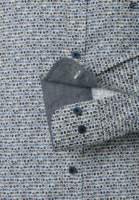 Button-up shirt featuring a blue and cream geometric pattern, with a contrasting gray inner cuff and dark buttons. Soft fabric texture.