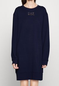 Mörkblå sweatshirtklänning, långa ärmar, rundad halsringning. Har en upphöjd 'EA7'-logotyp i rhinstenar på bröstet. Mjuk tyg, avslappnad passform.